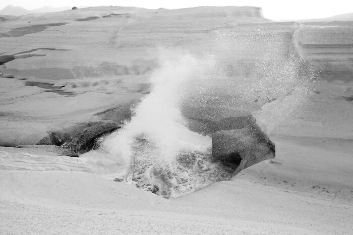 Black and white cinematic photo of ocean waves crashing against rocky cliffs capturing everyday life in nature.