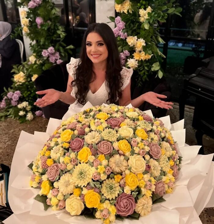 Woman smiling behind a large bouquet of baked goods that look like flower bouquets with pastel yellow and purple tones.