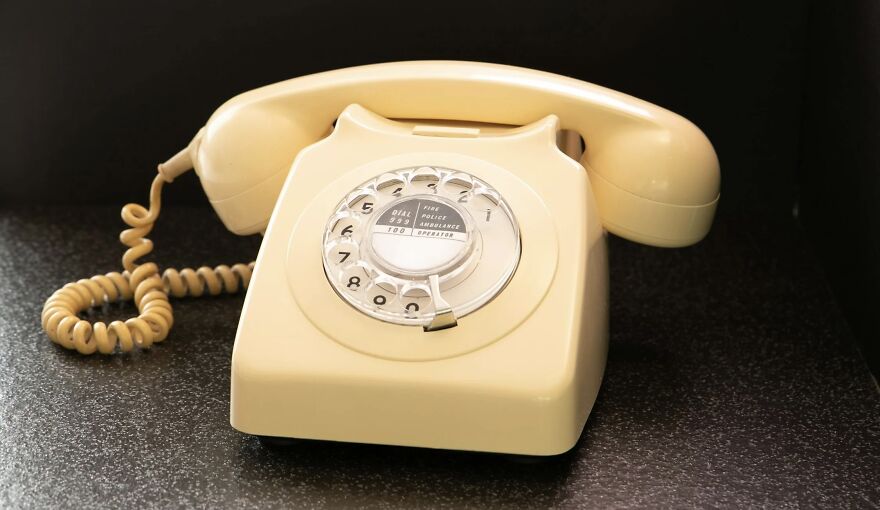 Beige rotary dial vintage telephone on a dark countertop symbolizing then vs now poll concept.
