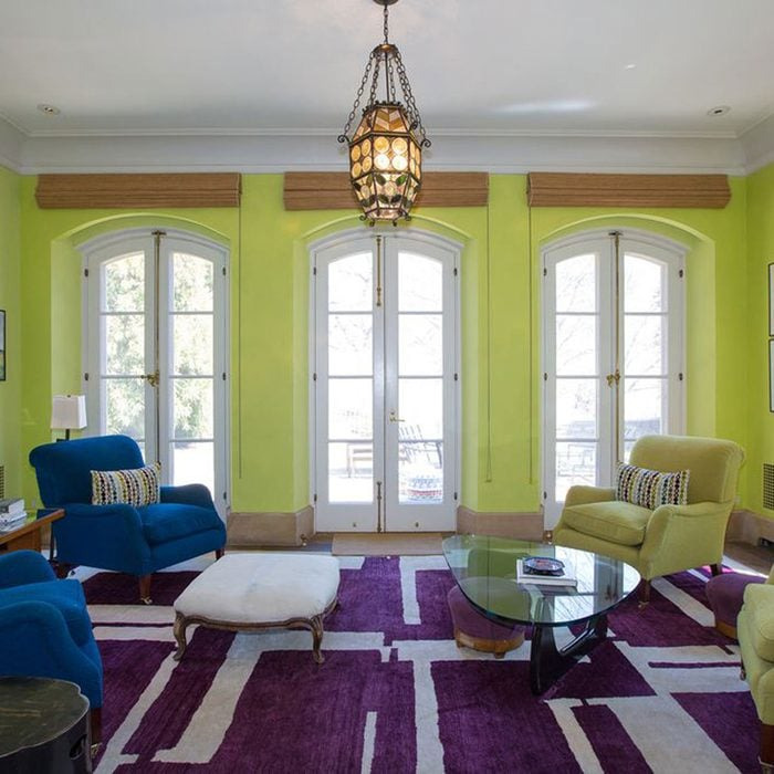 Living room with bright lime green walls, mismatched furniture, and a bold purple patterned rug in eccentric real estate listing.