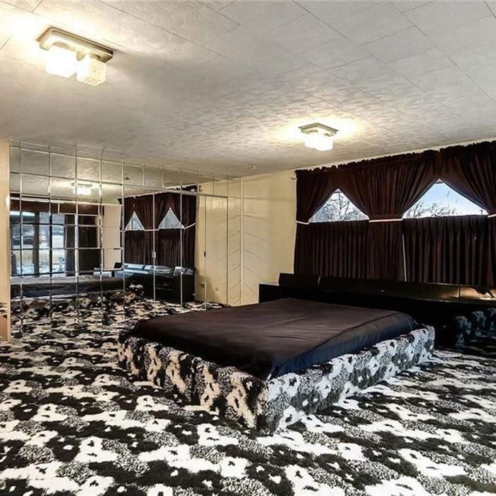 Bedroom with black and white patterned carpet and bed, dark curtains, and mirrored wall in unusual real estate listing.