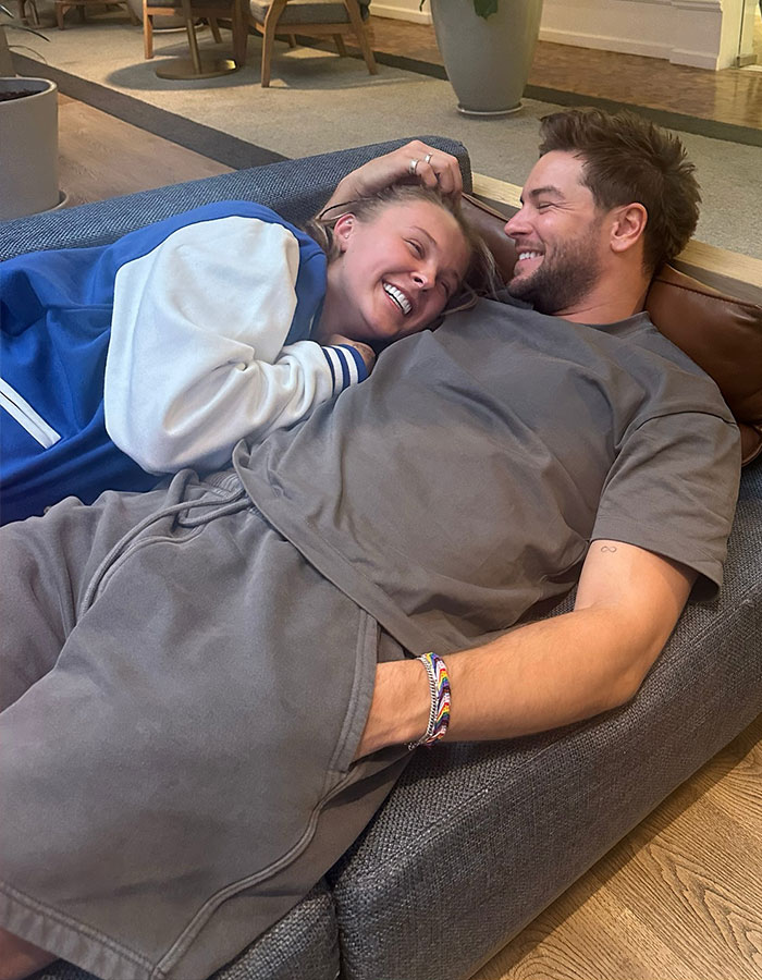 JoJo Siwa smiling and relaxing on a couch with a man, showcasing a casual and happy moment together. JoJo Siwa smiling and relaxing on a couch with a man, showcasing a casual and happy moment together.