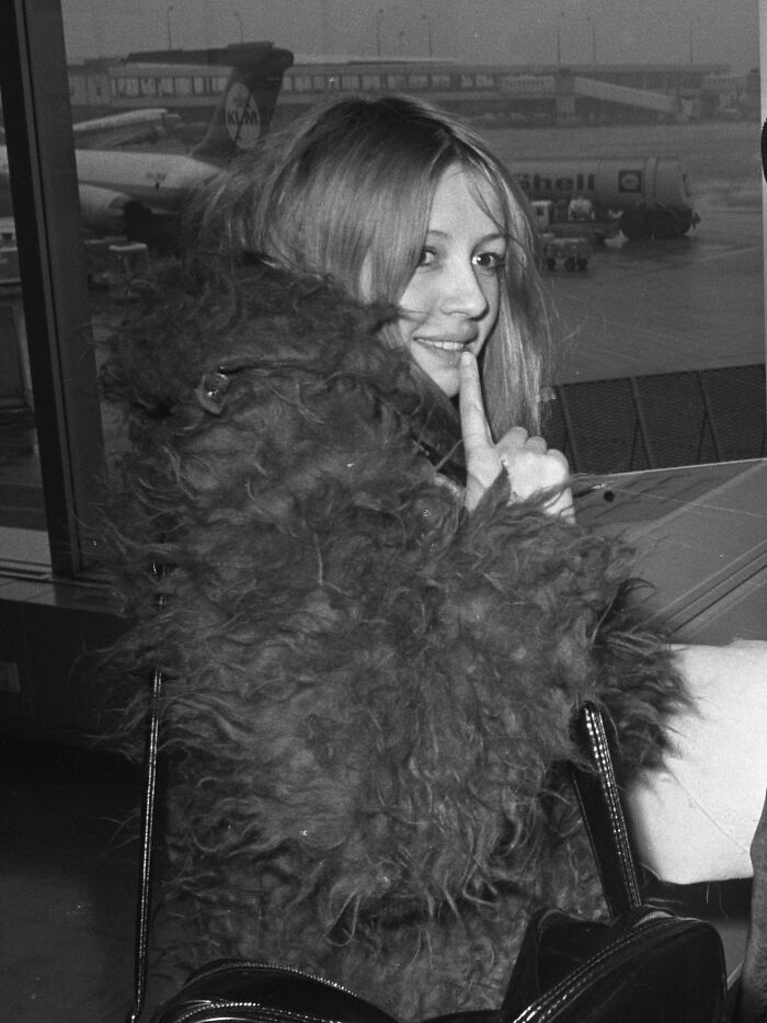 Young female star at airport wearing a fur coat, captured candidly in a moment reflecting stars we lost too soon.
