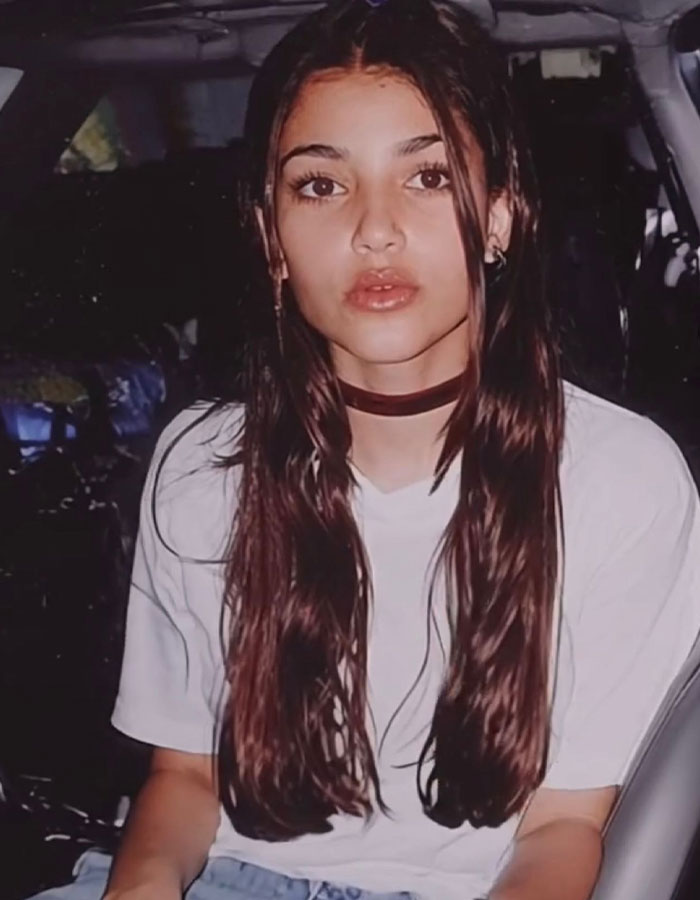 Young woman with long brown hair and choker sitting in a car, linked to Kim Kardashian throwback and plastic surgeries discussion.