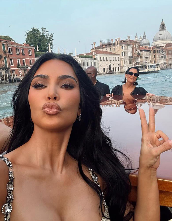 Kim Kardashian posing on a boat with Venice canals in the background, showcasing her glamorous look ahead of Bezos pajama party.