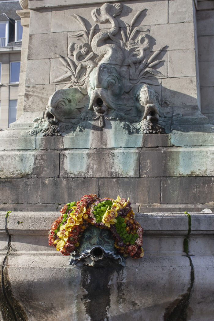 City statue adorned with colorful flowers, showcasing artistic floral decoration on urban stone sculpture detail.