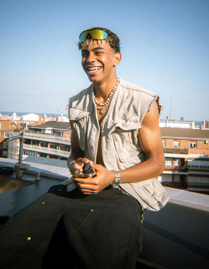 Young man smiling outdoors in sleeveless vest and sunglasses, related to fans finding old comment on thirst trap.