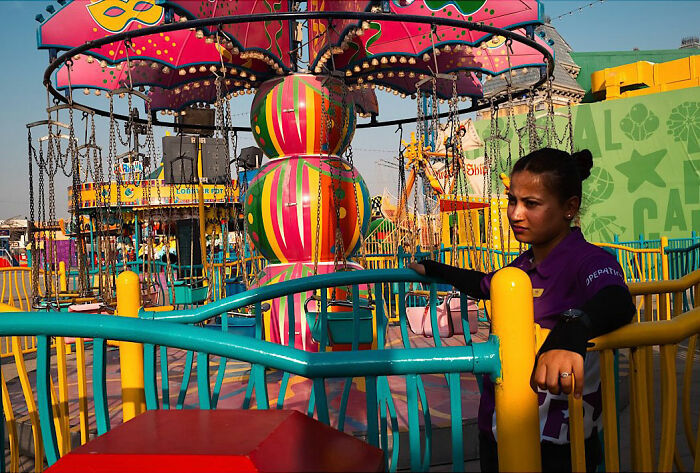 Woman working at a colorful carnival ride, captured as part of candid street moments full of emotion by traveling photographer.
