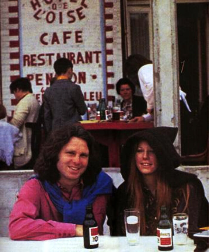 Last known photo of two famous people sitting at a cafe table with drinks, capturing a candid moment outdoors.