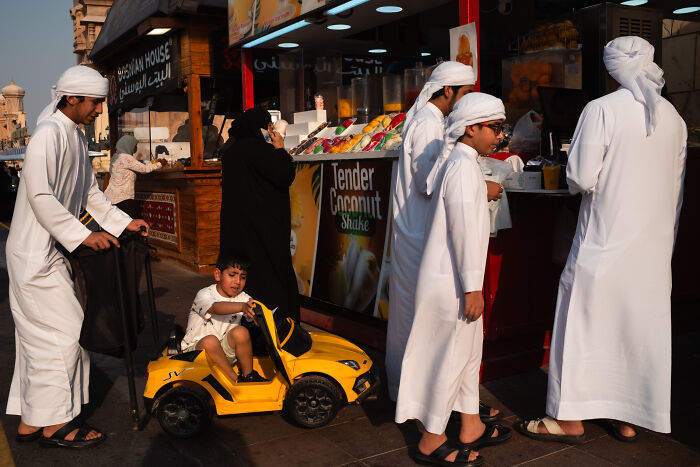 Child riding a yellow toy car in a candid street moment captured by photographer traveling the world full of emotion