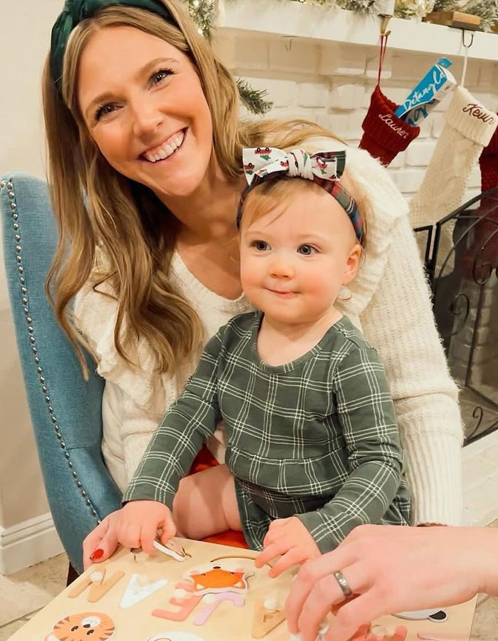 Smiling woman and toddler playing with a puzzle by the fireplace, illustrating real housewives exec and her two children.
