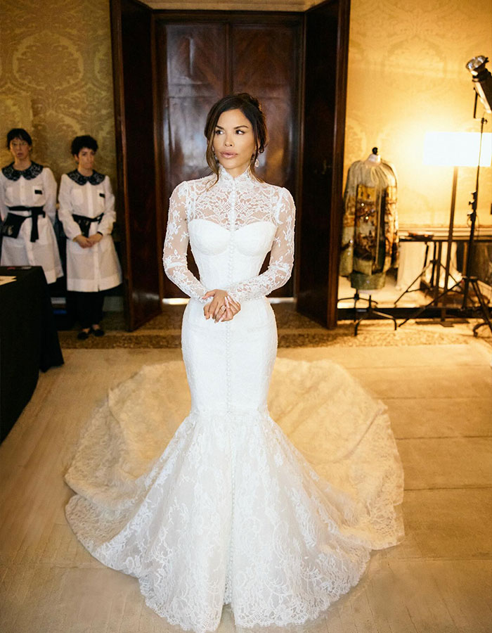 Lauren S&aacute;nchez in a white lace bridal gown poses while staffers photobomb uncomfortably in the background.