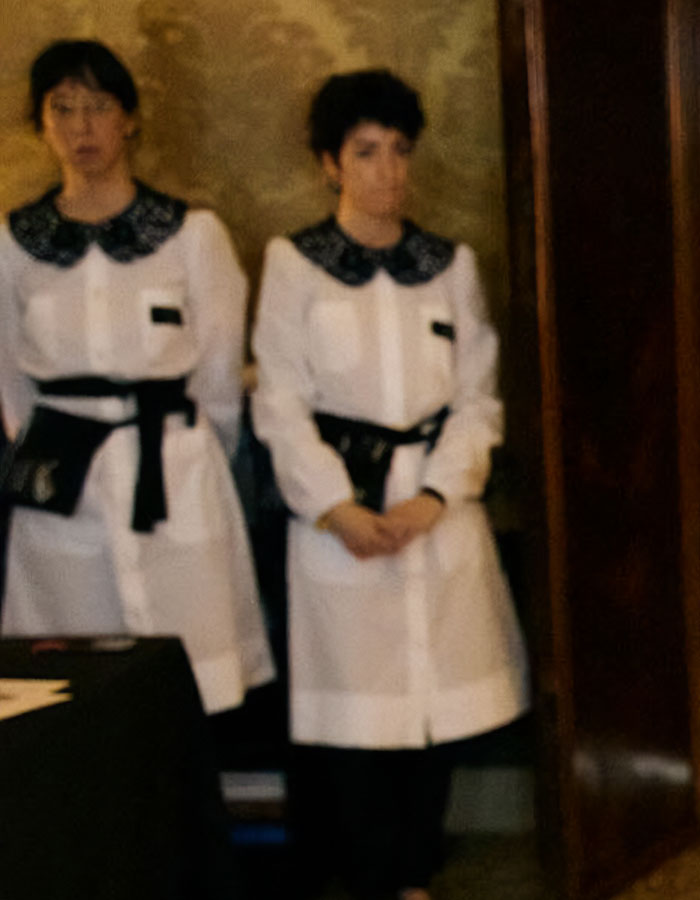 Two uncomfortable staffers dressed in uniforms standing against a wall, photobombing in a viral bridal pic.