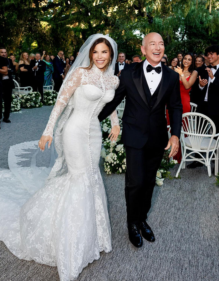 Lauren S&aacute;nchez in a white lace wedding dress showing blue veins on her hands at a celebratory outdoor wedding event.
