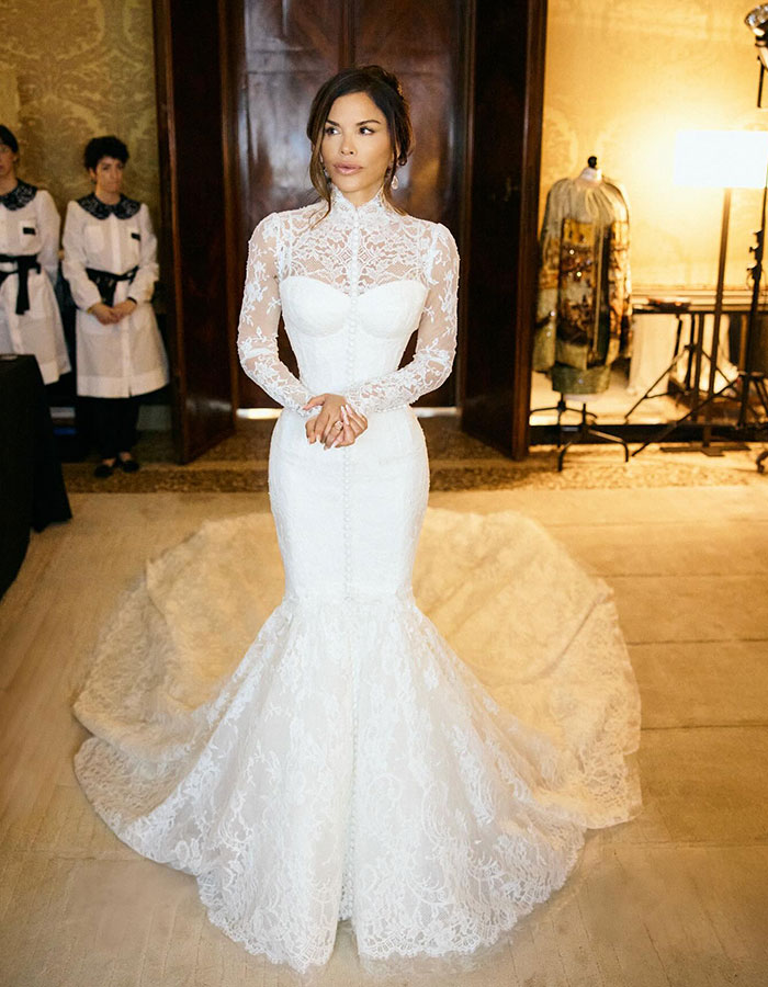 Lauren S&aacute;nchez in a white lace wedding dress, highlighting blue veins on her hands in an elegant indoor setting.