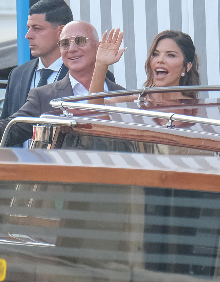 Lauren S&aacute;nchez waving from a boat, showing blue veins on her hands, sparking buzz and amusing comparisons outdoors.