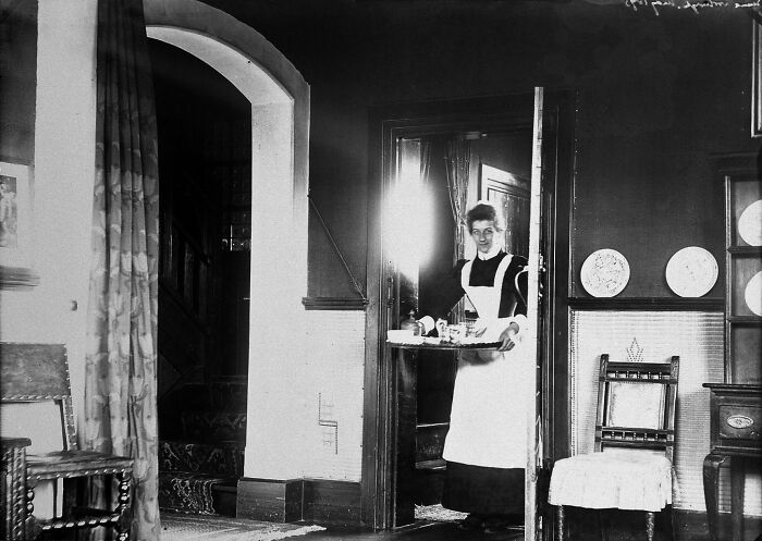Victorian maid carrying a tray through a doorway in a historic room, showcasing strange moments from Victorian times.