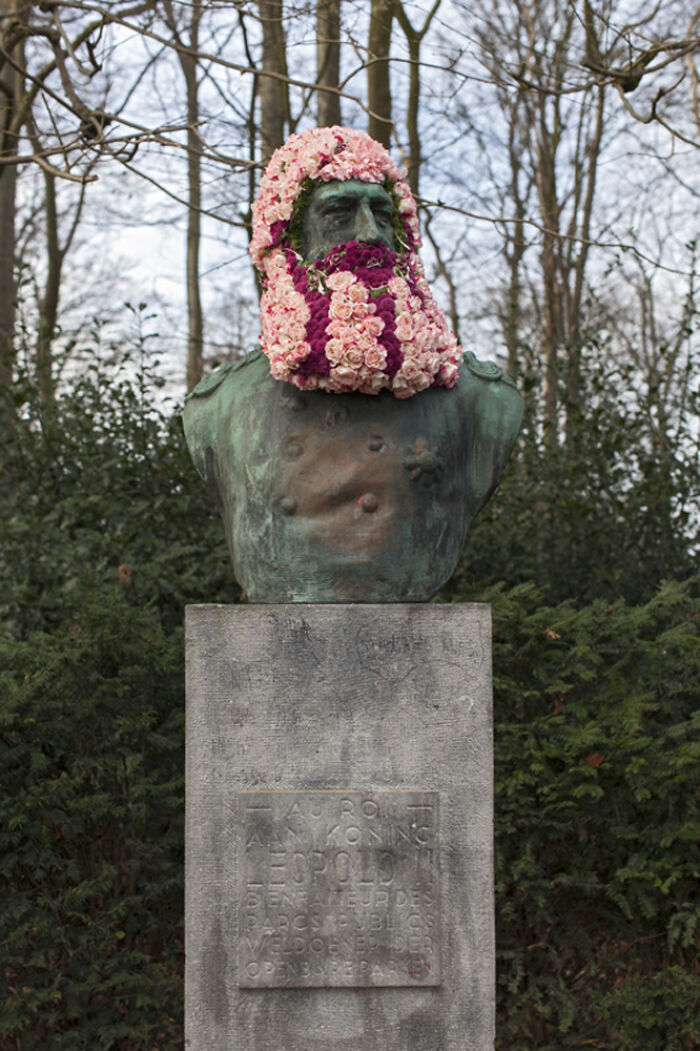 Statue in a city park dressed with flowers forming a colorful floral beard and hair by the artist.