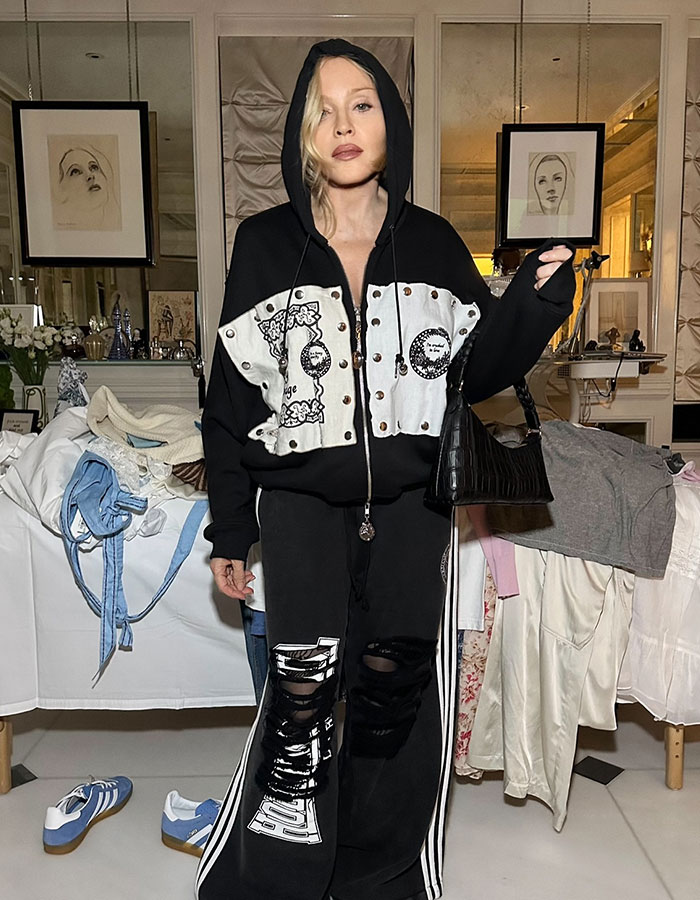 Madonna wearing a black hoodie and ripped pants, posing indoors amid clothes, linked to Hamilton star behavior controversy.