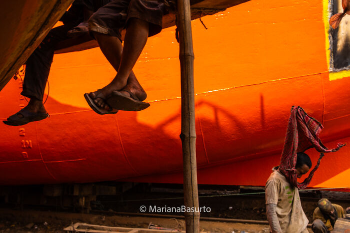 Feet of workers and a man cleaning near a bright orange boat, showcasing unseen realities captured by the photographer.