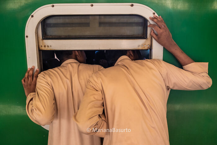 Two men lean through a small train window, capturing unseen realities in a vibrant, candid street photography shot.