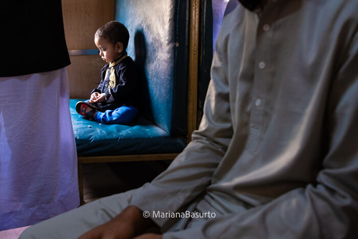Child sitting contemplatively on a blue bench revealing unseen realities in a candid photographer’s shot indoors.