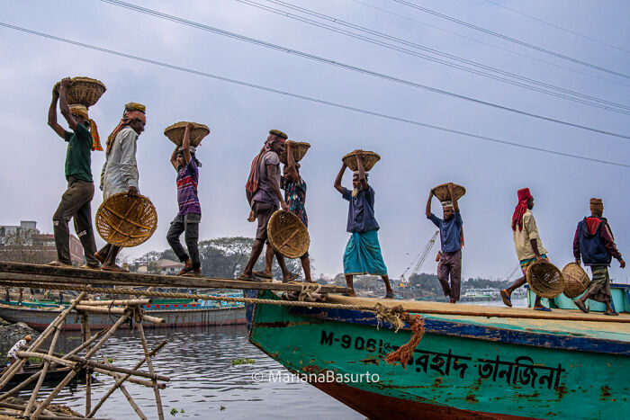 Workers carrying baskets across a wooden plank onto a boat, capturing unseen realities of our world through photography.