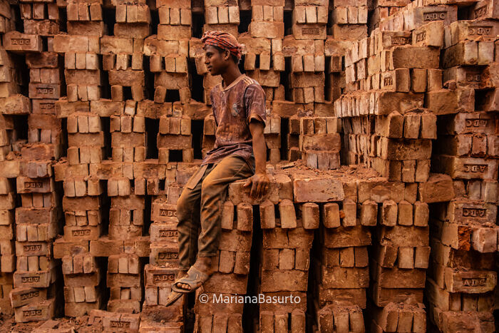 Young boy sitting on stacked bricks in a dusty environment, showcasing the unseen realities captured by a photographer.