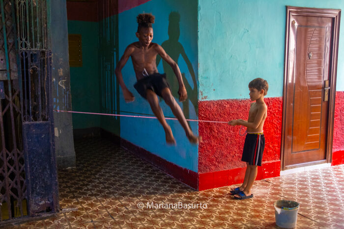 Two boys playing jump rope indoors, captured by a photographer revealing unseen realities of our world.