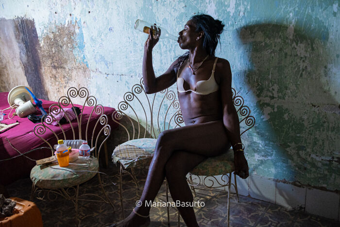 Woman in a dim room drinking from a bottle, capturing unseen realities of our world in a raw photographic moment.