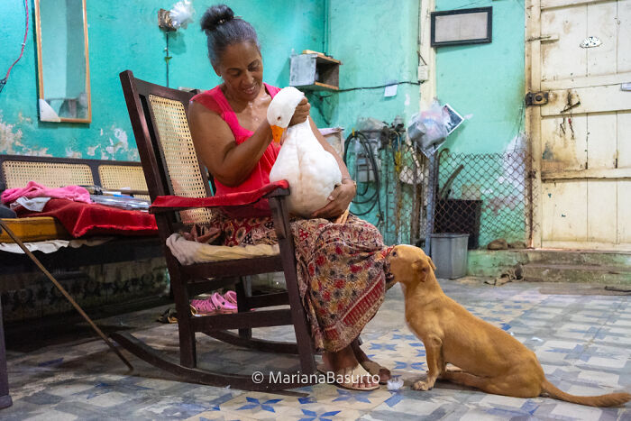 Woman holding a white duck in a rustic room while a small dog looks up, capturing unseen realities through photography.