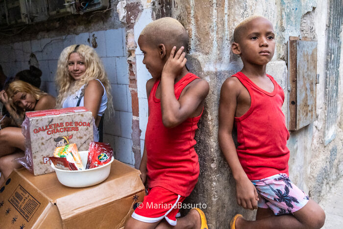 Two boys in red shirts leaning against a wall while two women sit in the background, capturing unseen realities of our world.