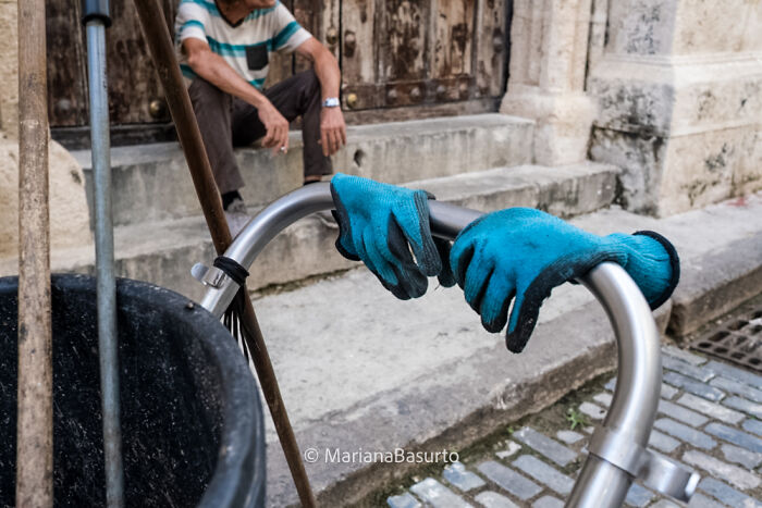 Blue gloves hanging on a metal handle with a man sitting on steps in the background, revealing unseen realities of our world.
