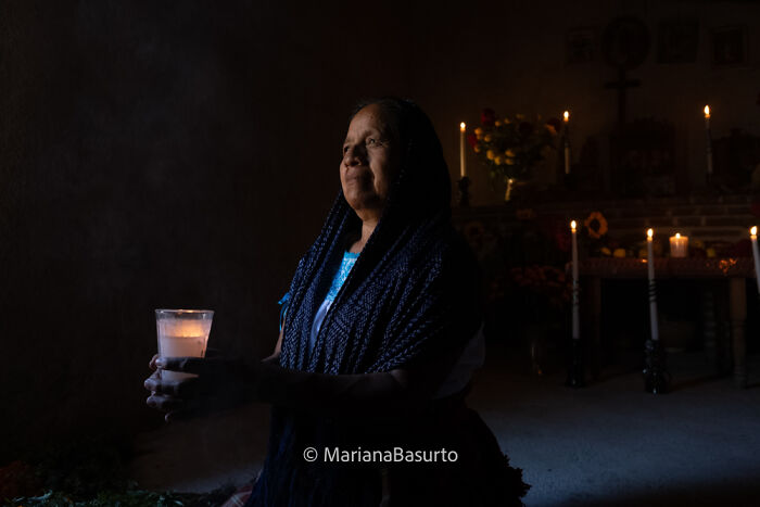 Woman holding a lit candle inside a dim room, capturing unseen realities of our world through powerful photography.