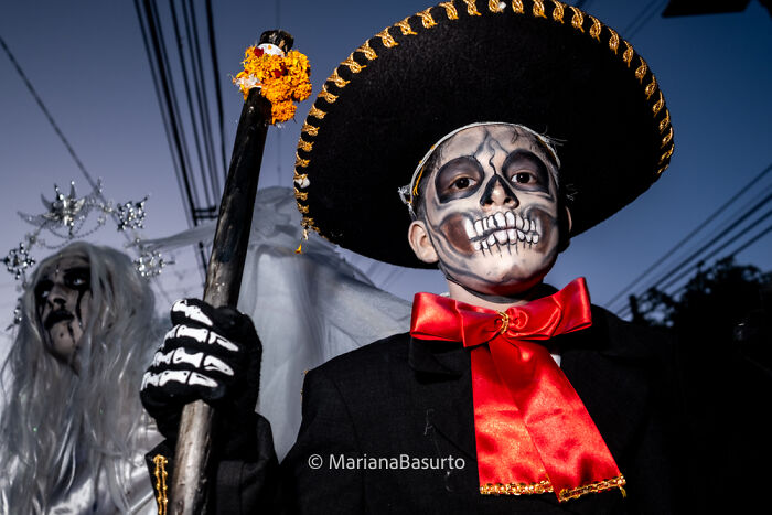 Child in Day of the Dead costume with skull face paint and traditional hat, showcasing unseen realities through powerful photography.