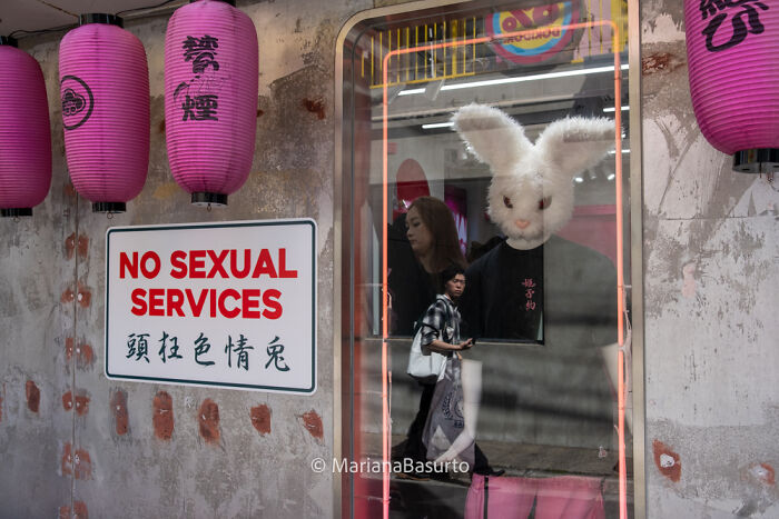 Street scene reflecting unseen realities featuring a person with a rabbit mask behind glass and a no s****l services sign.