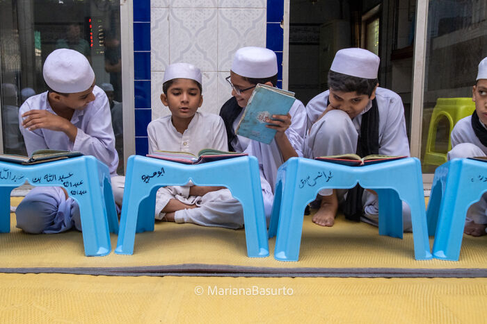 Young boys in traditional attire reading religious books seated behind blue stools, capturing unseen realities of our world.