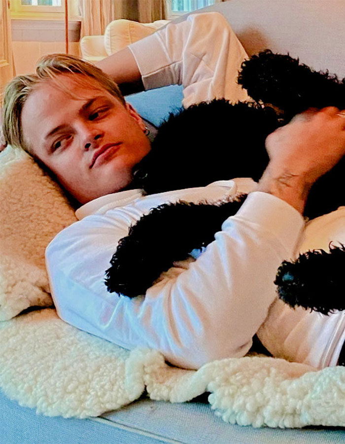 Norwegian Crown Princess&rsquo;s son lying on a couch, holding a black dog, in a relaxed indoor setting.