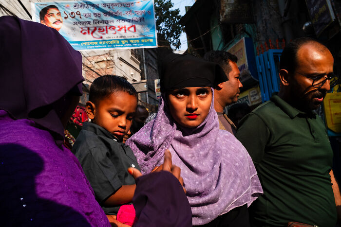 Woman in a purple hijab and black headscarf looking at the camera in a candid street moment full of emotion.
