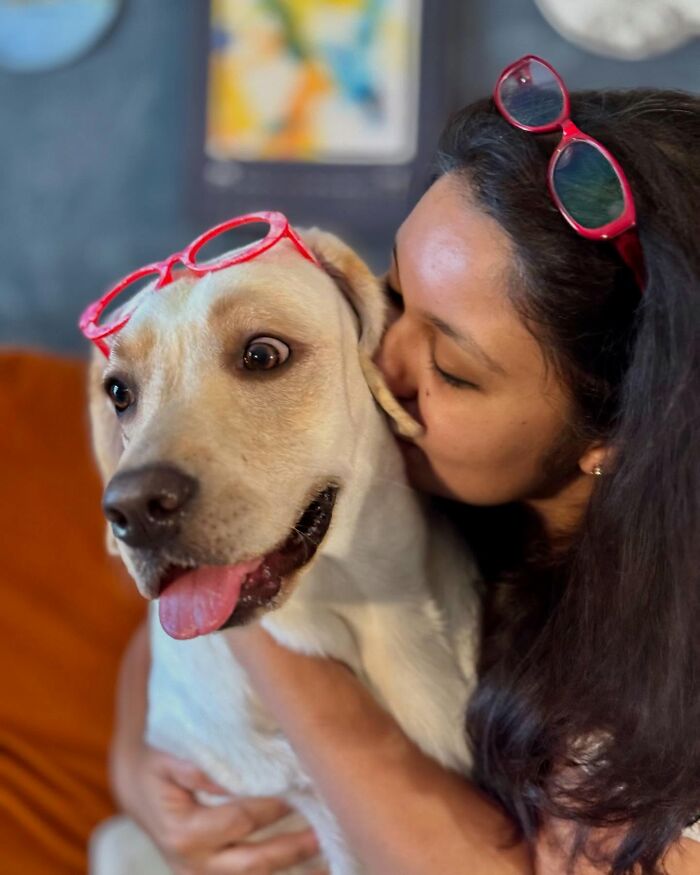 Woman hugging a rescue Labrador wearing red glasses, showcasing the Labrador's unique talent for painting with her mouth.