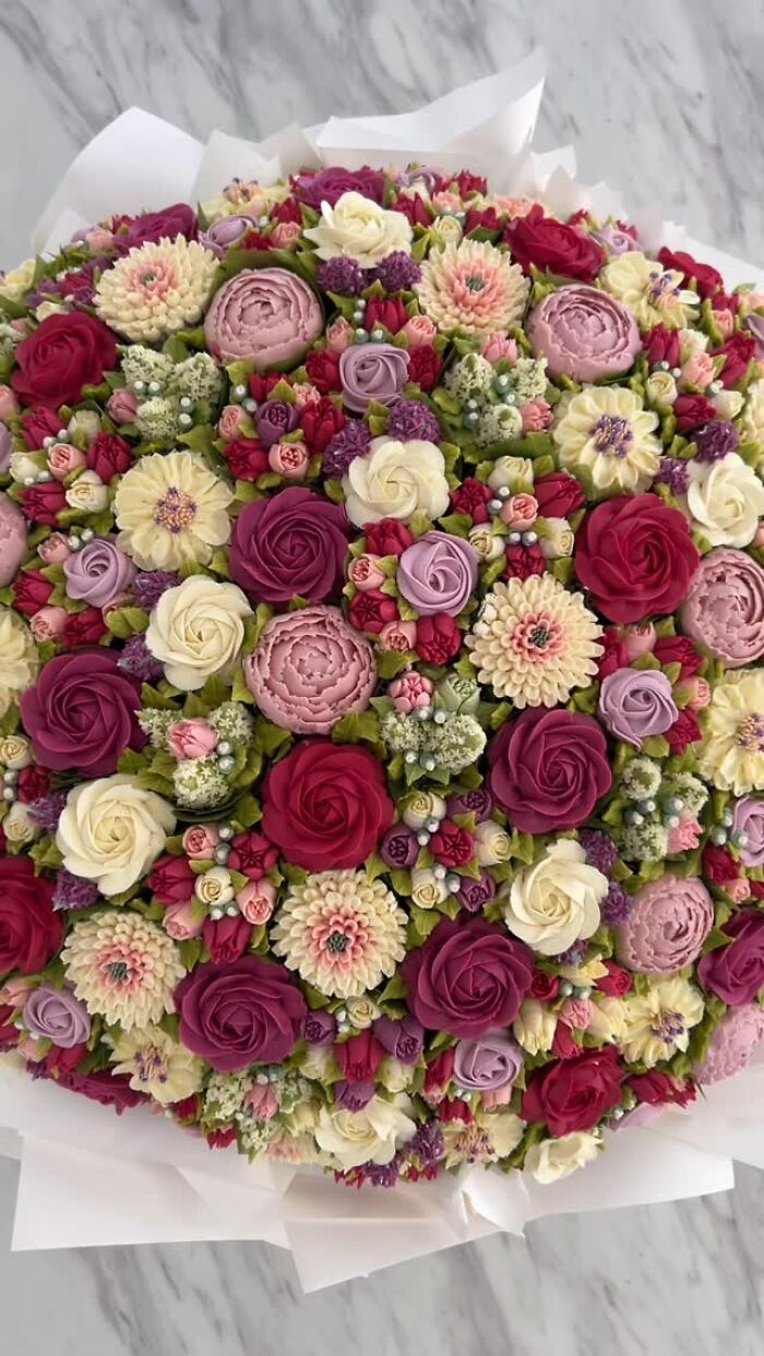 Colorful baked goods arranged to resemble a flower bouquet, showcasing intricate cupcake and floral designs by an artist.