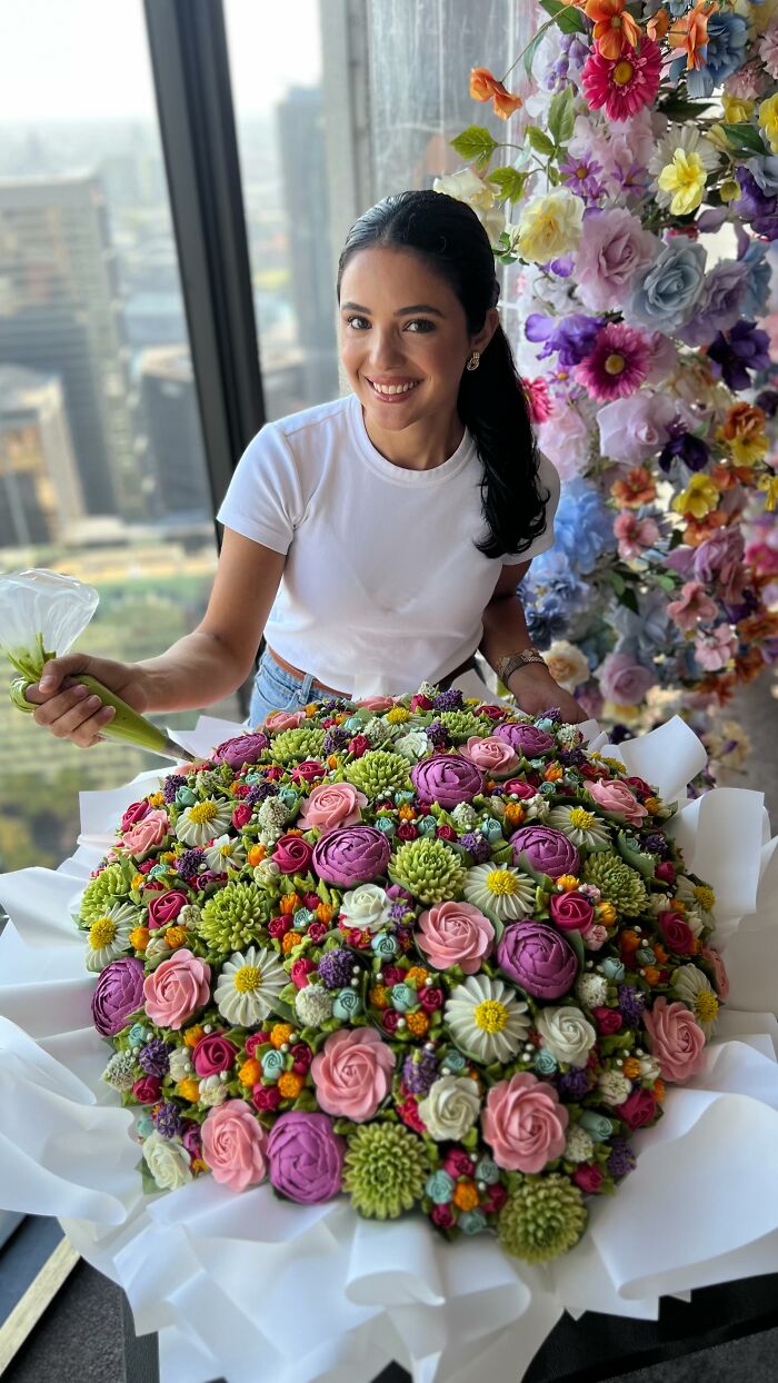 Woman decorating a large bouquet of baked goods that look like colorful flower cupcakes with icing details.