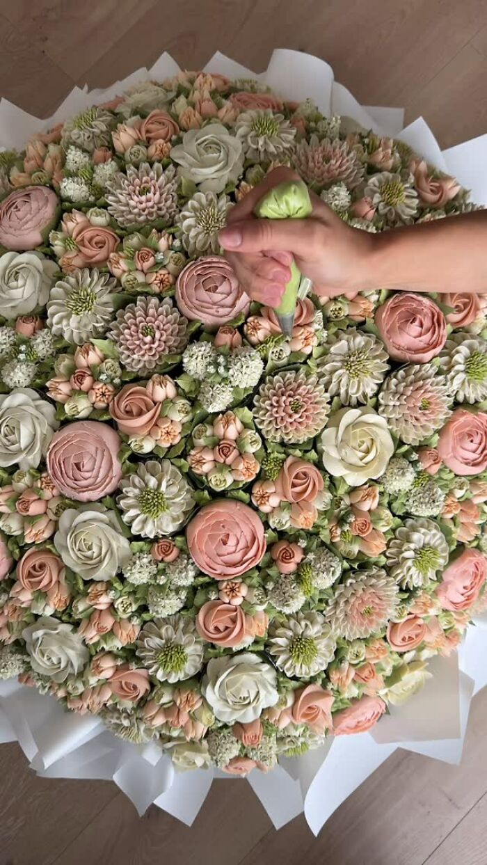 Hand piping intricate flower designs with pastel colors on baked goods resembling flower bouquets.