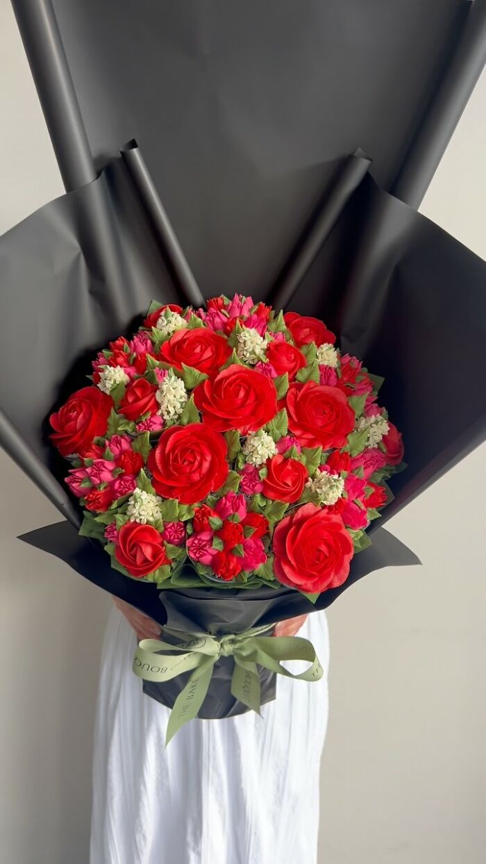 Bouquet of baked goods resembling vibrant red and pink flower arrangements wrapped in black paper with a green ribbon.