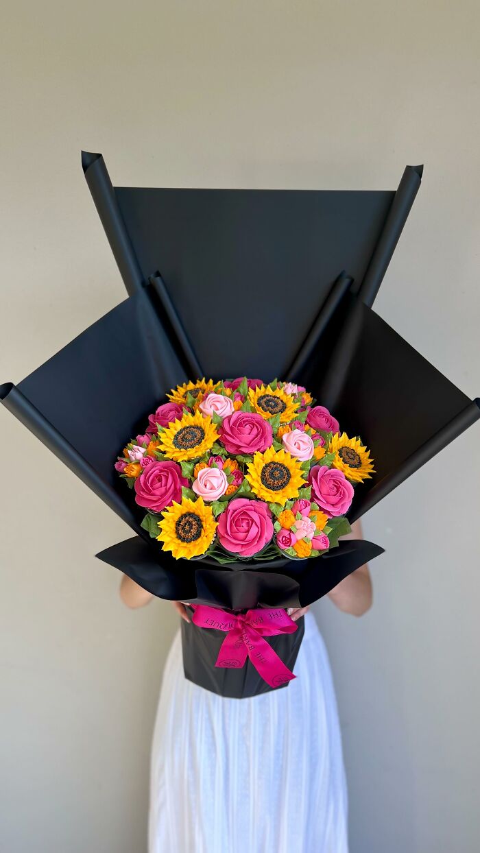 Bouquet of baked goods resembling sunflowers and roses wrapped in black paper, showcasing creative cupcake art design.
