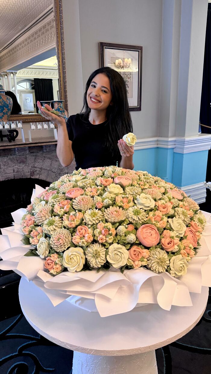 Woman holding a cupcake flower surrounded by a large bouquet of baked goods that look like flower bouquets on a table.