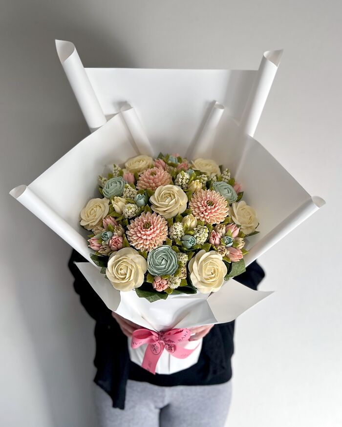 Bouquet of baked goods designed to look like flower bouquets with pastel pink, cream, and green frosting petals wrapped in white paper.
