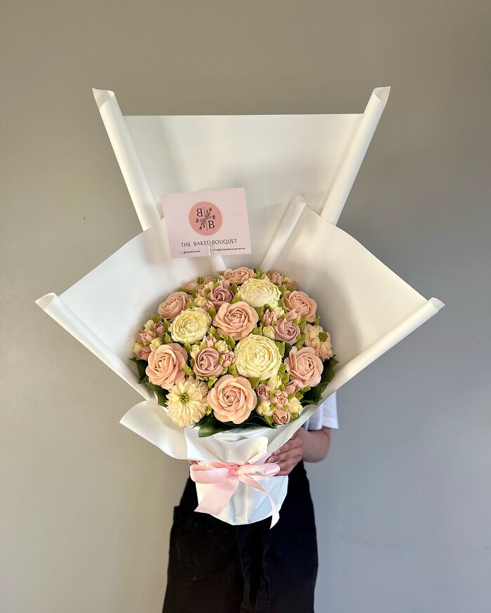 Bouquet of baked goods that look like delicate flower arrangements wrapped in white paper and held by a person.