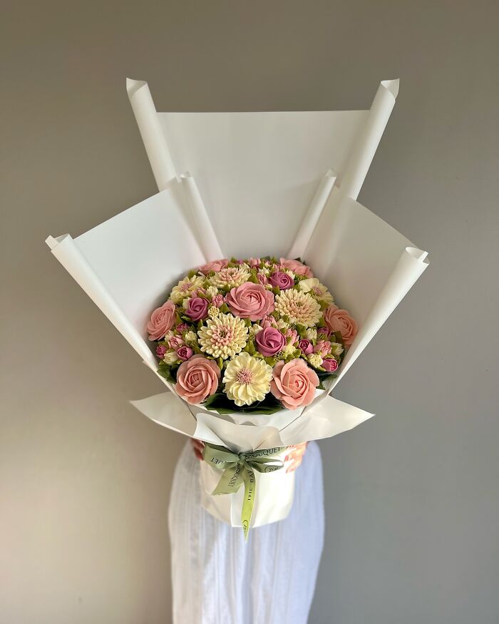 Bouquet of pastel flower cupcakes wrapped in white paper, showcasing baked goods that look like flower bouquets.