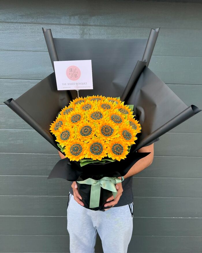 Bouquet of sunflower cupcakes designed as baked goods that look like flower bouquets, held by a person in casual clothes.